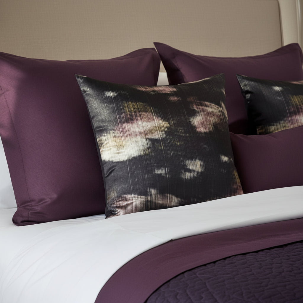 Decorative cushions with abstract pattern on a white and aubergine bedding