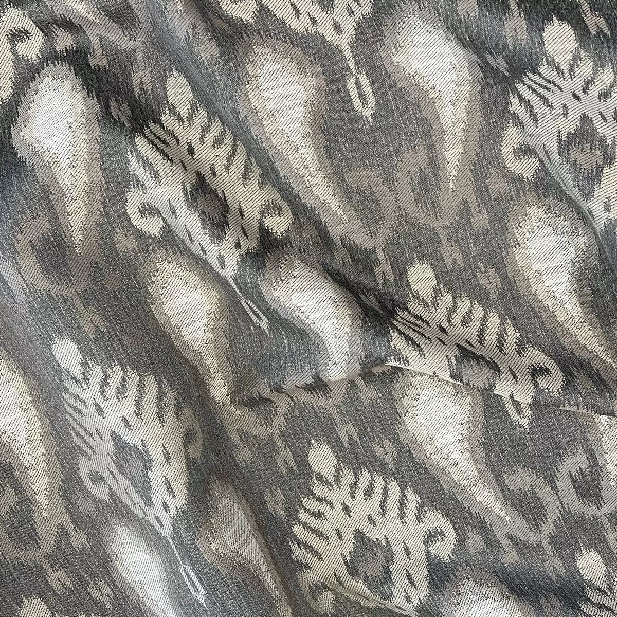 A close-up of draped fabric with an ikat-style pattern in grey, taupe and off-white.