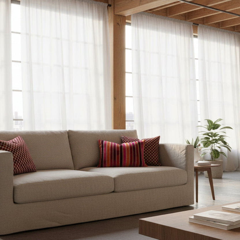 Beige sofa with patterned cushions in a bright living room with large windows.
