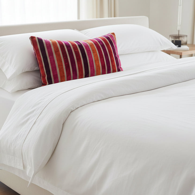 Striped lumbar cushion with red, orange, and purple colours on white bedding.
