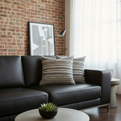 Two striped cushions sitting on a modern black sofa - in front of a brick feature wall.