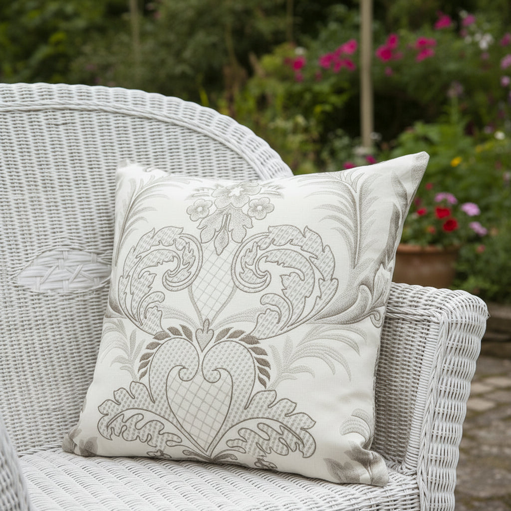 Decorative cushion with intricate damask pattern sitting on a white rattan chair  