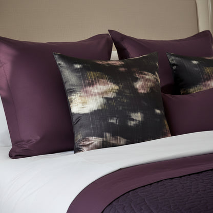 Decorative cushions with abstract pattern on a white and aubergine bedding 
