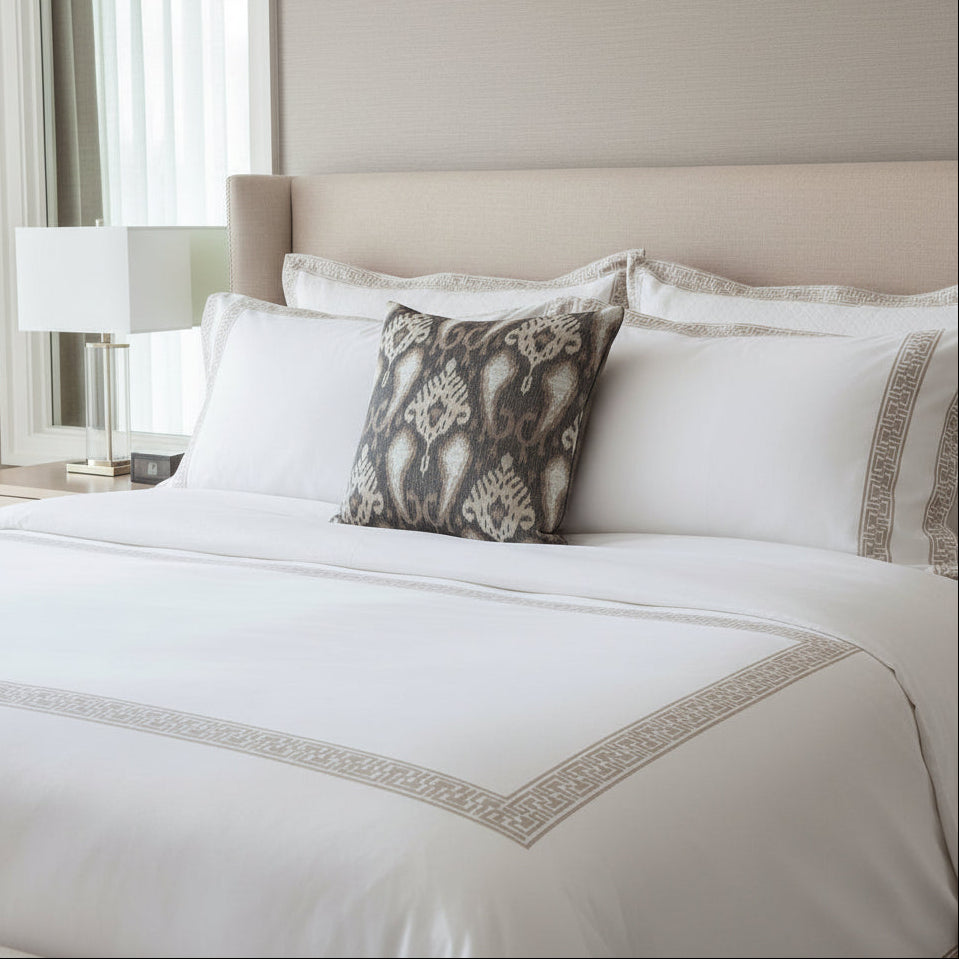 Neatly made bed with white bedding and decorative cushion in a bedroom setting.