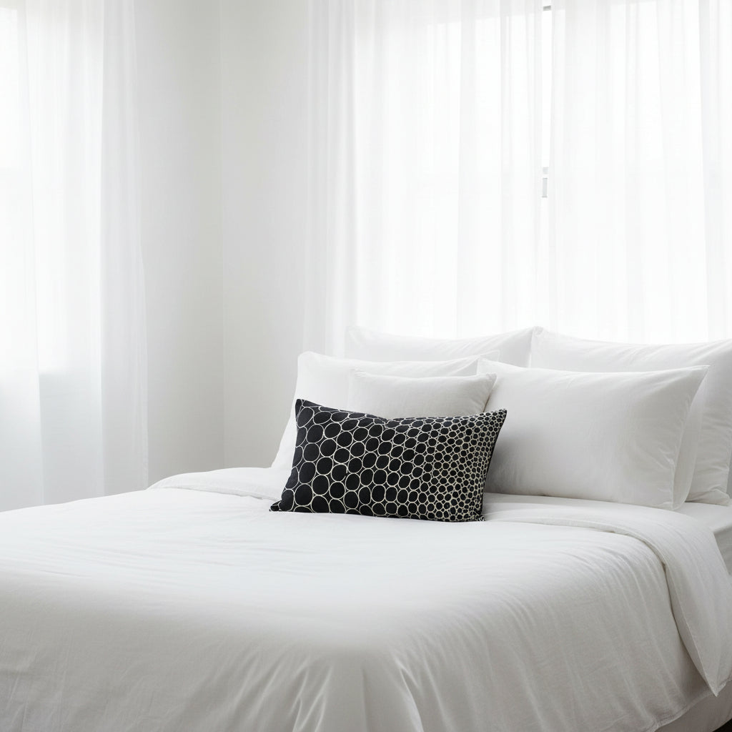 Black and white circle patterned cushion, sitting on white bedding in a white room 