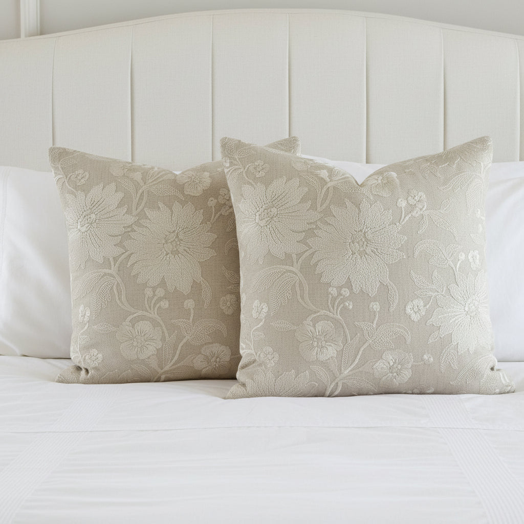 Two decorative embroidered cushions on white bedding   