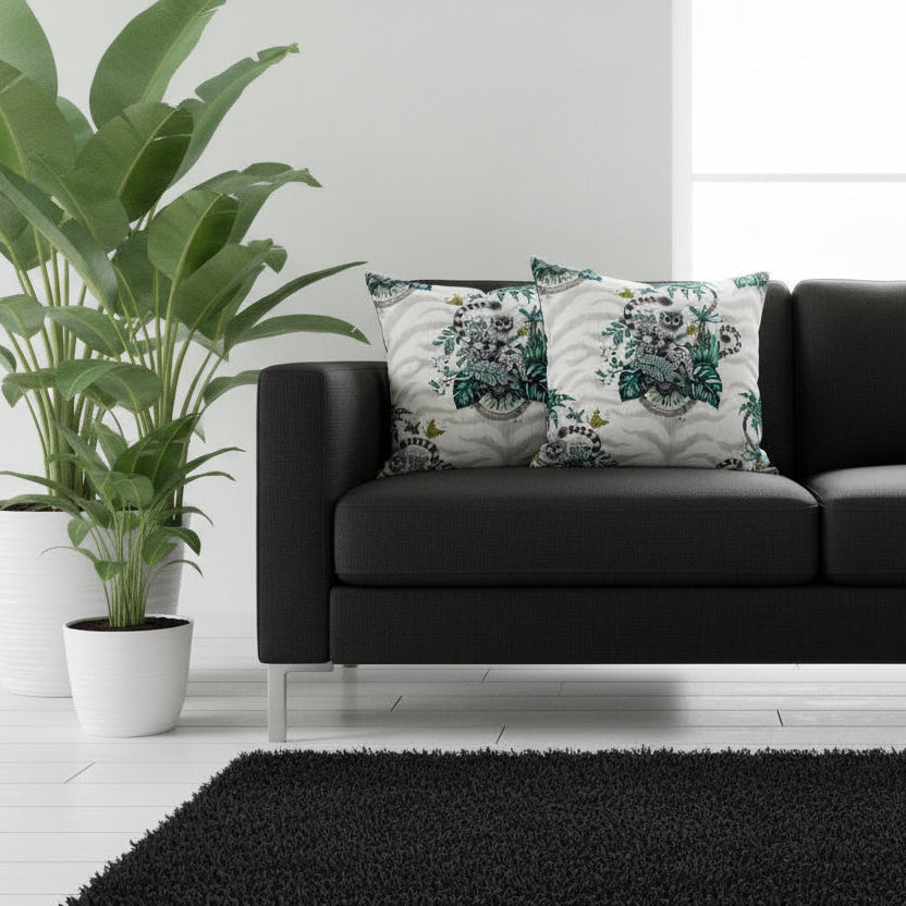 Black sofa with decorative pillows in a living room setting with plants and a rug.