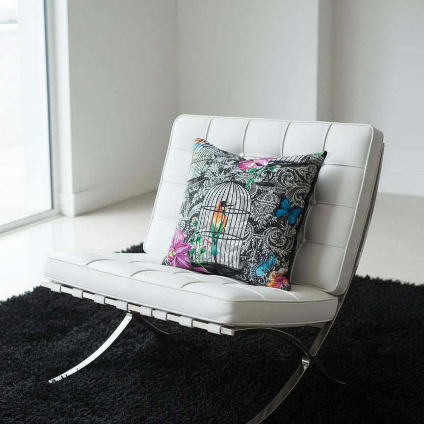 White Barcelona Chair with a decorative cushion on a black rug in a white room with windows.