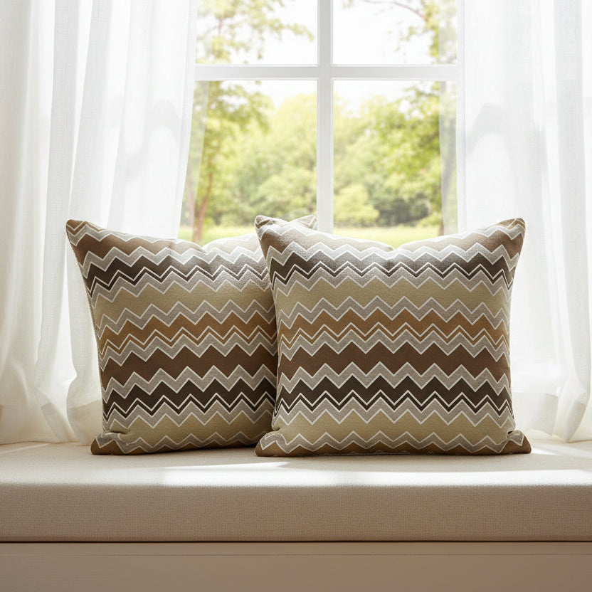 Two zig zag patterned cushions on a window seat with white curtains.