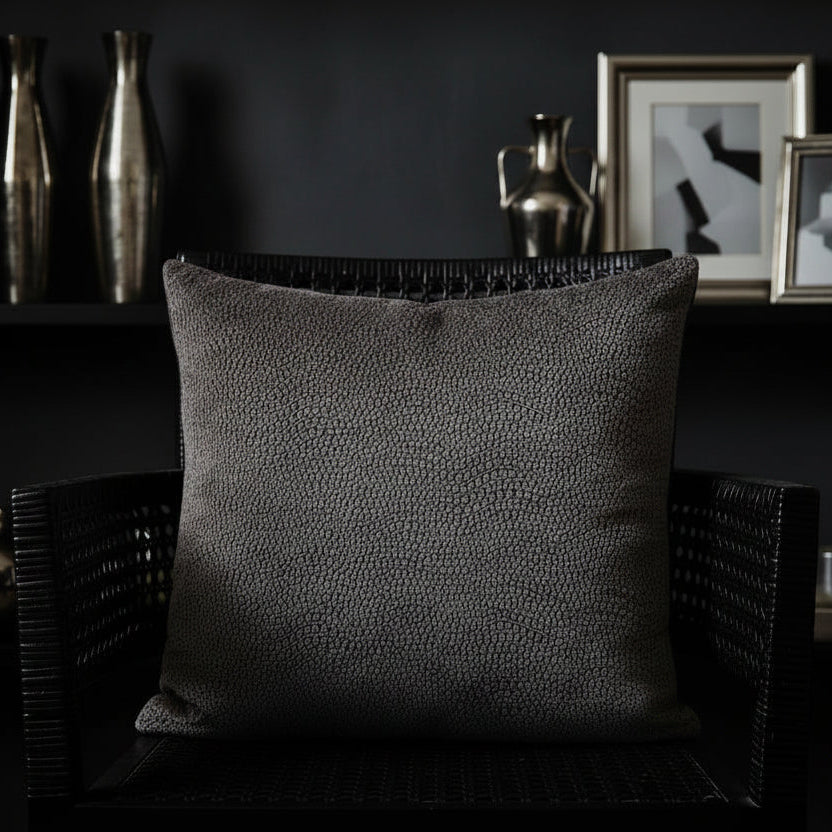 Textured cushion a dark wicker chair with decorative vases and framed pictures in the background.