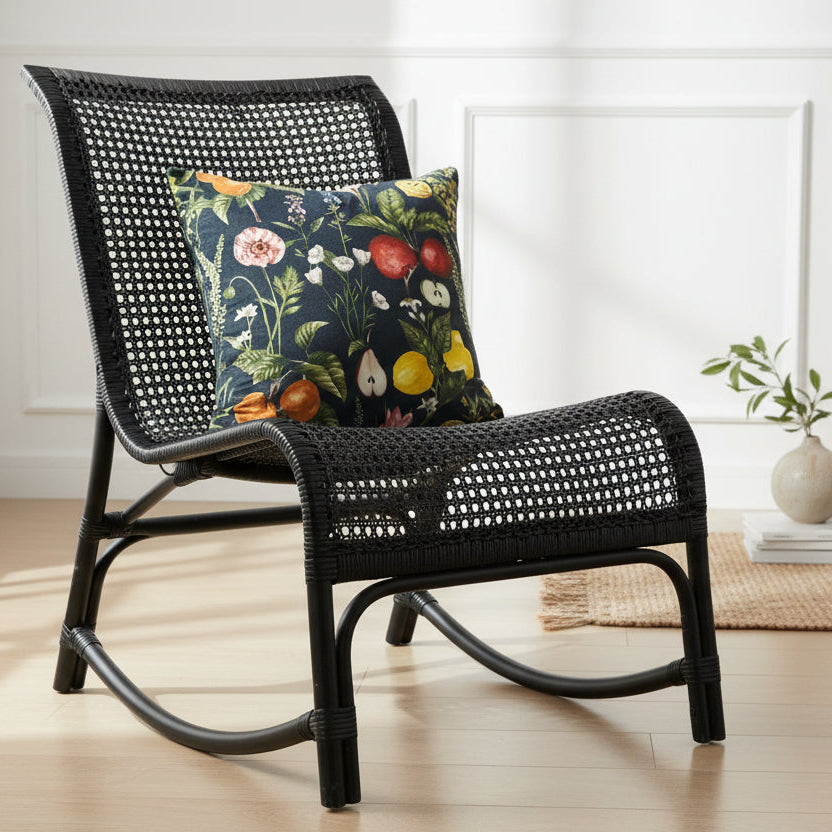 Black wicker chair with a decorative cushion in a room with light wood flooring and white walls.