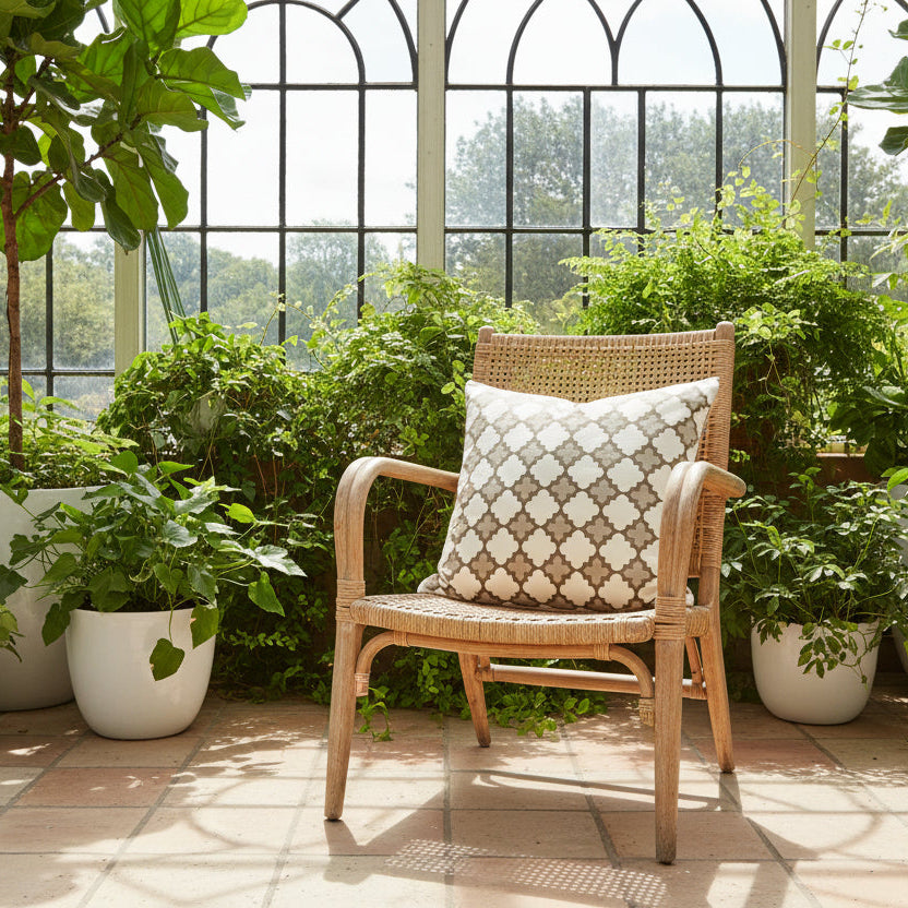 Wicker chair with a patterned cushion in a sunlit conservatory, filled with potted plants.