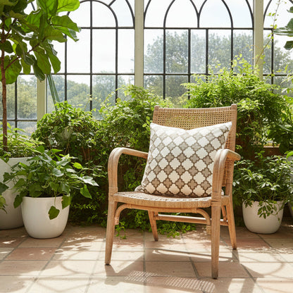 Wicker chair with a patterned cushion in a sunlit conservatory, filled with potted plants.