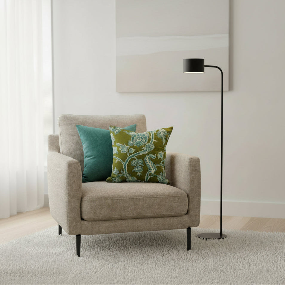 Beige armchair with green and blue patterned cushions in a room with a lamp and white wall.