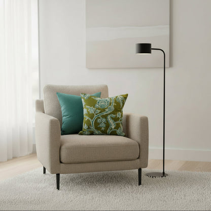 Beige armchair with green and blue patterned cushions in a room with a lamp and white wall.