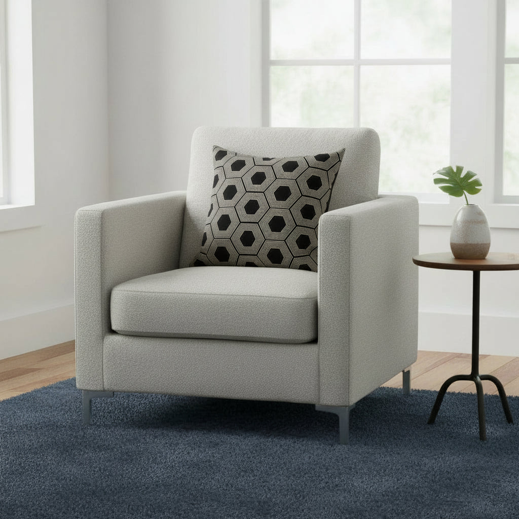 Gray armchair with a patterned pillow in a room with a small table and plant.