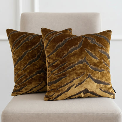 Two gold bengal tiger stripe patterned cushions sitting on a neutral chair and a white background
