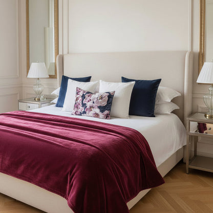 Neatly made bed with decorative cushions and a deep pink throw blanket in a well-lit bedroom.