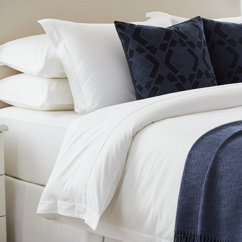 Bedroom setting with white bedding and navy blue cushions and coordinating throw blanket.