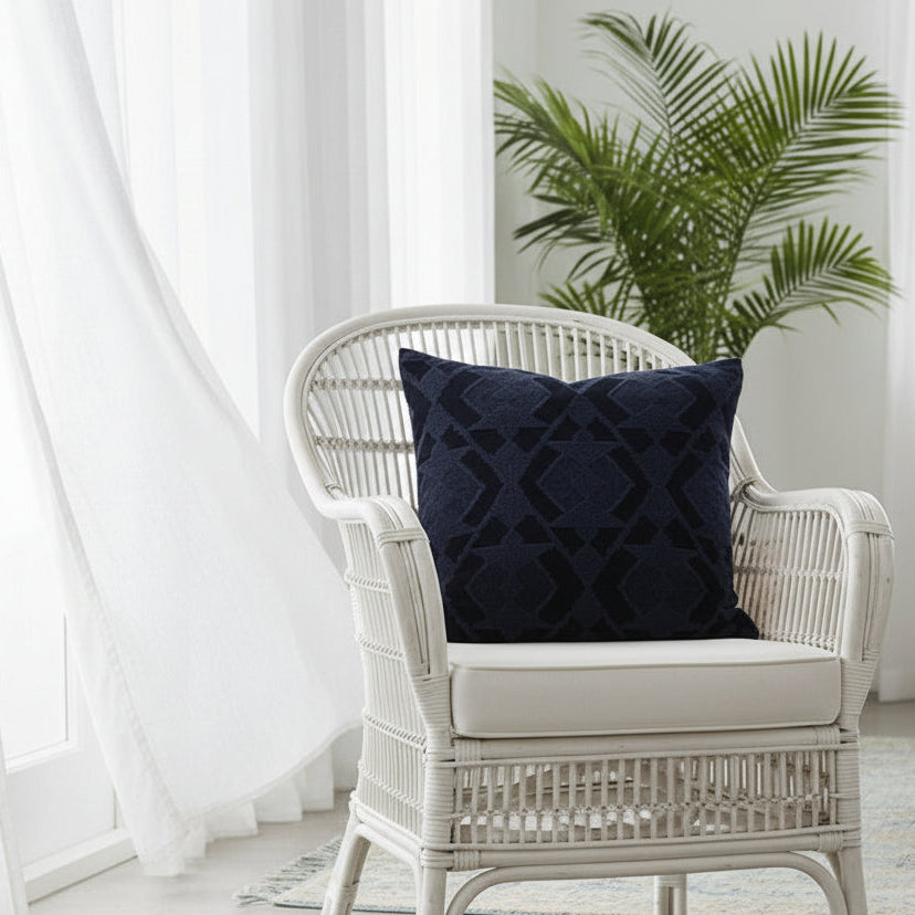 White wicker chair with a navy blue patterned cushion in a bright room with white curtains and a plant.